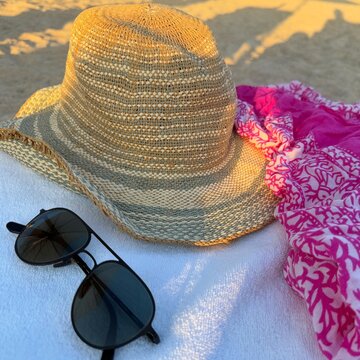 Close-up of a straw sun hat, sunglasses and sarong on a sun lounger on a beach
