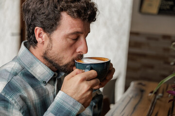 A young man enjoys a cup of specialty coffee with latte art to unwind from the work day. Copy space, close up.