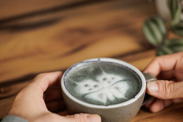 Man with a matcha latte in his hands with a butterfly drawing, enjoys specialty coffee in a cafe and takes a break.