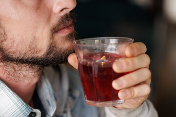A man smiles while holding a cup of red fruit tea, he enjoys the aroma of the infusion while relaxing after a long day at the office or at the university.