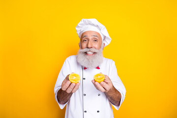 Smiling senior chef holding lemon halves in front of yellow background, representing culinary...