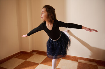 Young girl practicing ballet in a brightly lit room in elegant dancewear