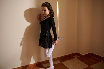 Young dancer stretching leg against wall at home in natural light
