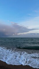 Ocean waves gently washing over the shore under a vast blue sky, with soft clouds creating a tranquil seascape