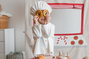 Smiling girl pretending to be a pastry chef covered her eyes with freshly baked bagels