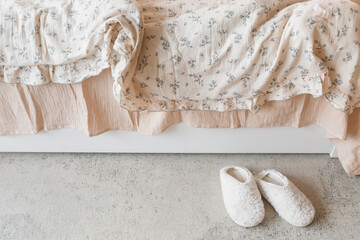 Overhead view of a pair of cosy slippers next to an unmade bed in a bedroom