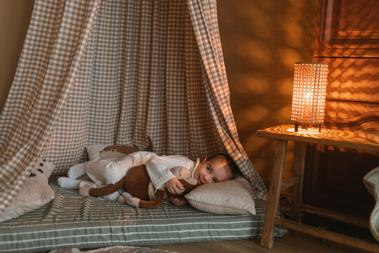 Smiling girl in pyjamas lying on her side in a teepee cuddling a toy monkey