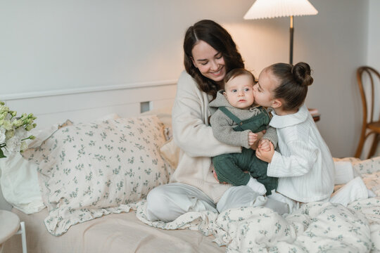 Smiling young woman sitting in bed with her young daughter kissing her son on the cheek