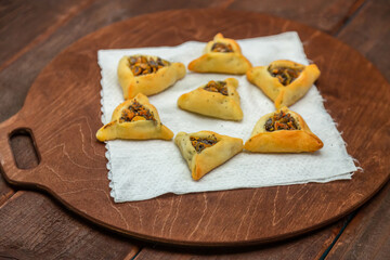 Sweet pastries triangular gomentashi for Purim on a wooden board on a napkin laid