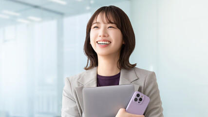 パソコンとスマホを持つ笑顔の若い女性・ビジネスウーマン