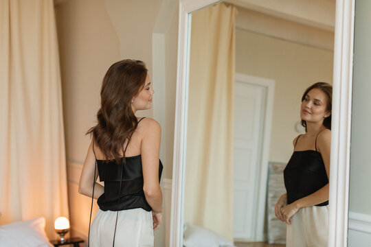Stylish young woman standing in front of a mirror in her bedroom looking at her reflection
