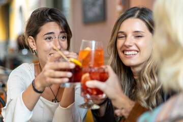 Young women toasting with Aperol Spritz and cocktails at a café - socializing at celebration party