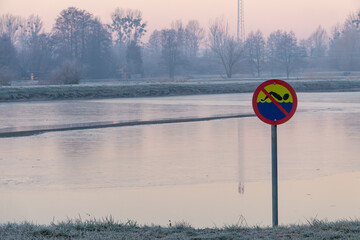 the sun rising over the lake. winter countryside landscape. a sign prohibiting bathing and swimming in the retention water reservoir. compensation lake.
