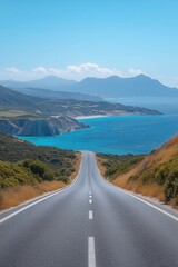 Obraz premium Endless road stretches towards vibrant turquoise sea, flanked by lush greenery and rugged cliffs, under a clear blue sky. Mountains in the distance add depth to the breathtaking landscape