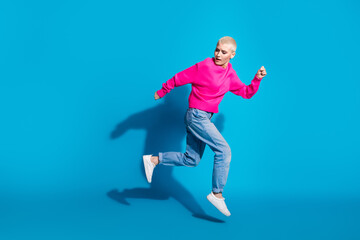 A young woman in a vibrant, pink pullover and casual jeans jumps energetically against a bright...