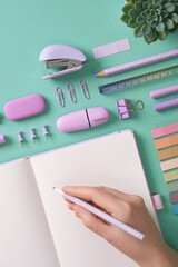 Blank notepad page for your text in pastel colored stationery frame. A woman is writing with a pen....