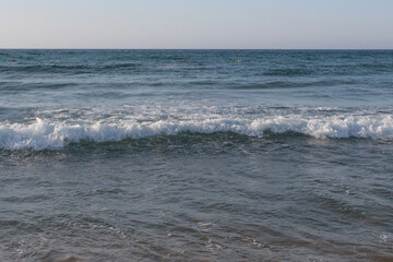 Beach of luxury hotel. sunny day, windy, stormy, wavy sea, blue sky. On the beach shines soft yellow-gold brown-golden sand. Sea waves crashing on the shore with wavy white foam. on island of cyprus
