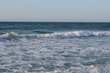 Beach of luxury hotel. sunny day, windy, stormy, wavy sea, blue sky. On the beach shines soft yellow-gold brown-golden sand. Sea waves crashing on the shore with wavy white foam. on island of cyprus
