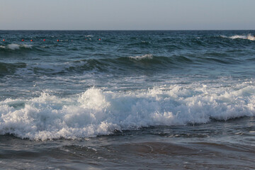 Beach of luxury hotel. sunny day, windy, stormy, wavy sea, blue sky. On the beach shines soft yellow-gold brown-golden sand. Sea waves crashing on the shore with wavy white foam. on island of cyprus
