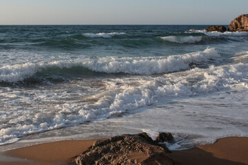 Beach of luxury hotel. sunny day, windy, stormy, wavy sea, blue sky. On the beach shines soft yellow-gold brown-golden sand. Sea waves crashing on the shore with wavy white foam. on island of cyprus
