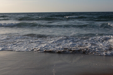 Beach of luxury hotel. sunny day, windy, stormy, wavy sea, blue sky. On the beach shines soft yellow-gold brown-golden sand. Sea waves crashing on the shore with wavy white foam. on island of cyprus
