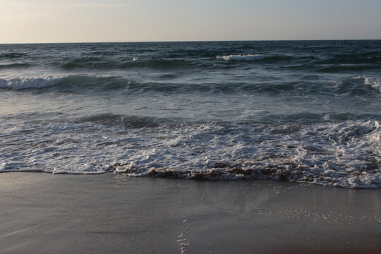 Beach of luxury hotel. sunny day, windy, stormy, wavy sea, blue sky. On the beach shines soft yellow-gold brown-golden sand. Sea waves crashing on the shore with wavy white foam. on island of cyprus
