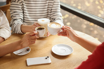 Women with cups of delicious coffee drinks at wooden table in cafe, closeup