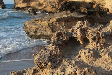 Beach of luxury hotel. sunny day, windy, stormy, wavy, large rocks in sea, blue sky. shines soft yellow-gold brown-golden sand. Sea waves crashing on the shore with wavy white foam. island of cyprus