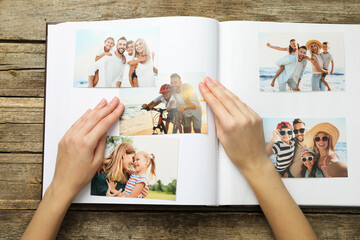 Woman with different photos in open photo album at wooden table, top view
