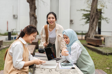 Multicultural women collaborating on project with laptop and notebooks outdoors at university.