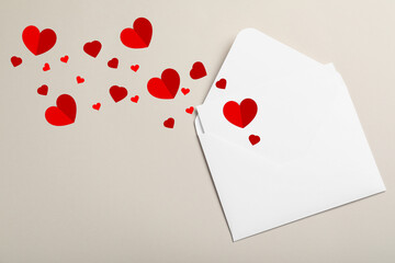 Red paper hearts flying out of envelope on beige background, top view. Love letter