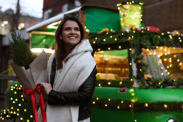 Happy woman with thuja tree near Christmas bus outdoors. Space for text