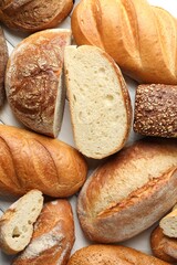 Whole and cut bread loafs on white table, flat lay