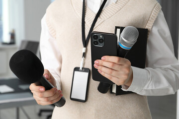 Journalist with microphones, smartphone and notebook indoors, closeup