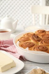 Freshly baked cinnamon rolls and ingredients on light wooden table indoors, closeup