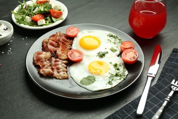 Tasty brunch. Delicious fried eggs, bacon, salad and glass of juice served on black table