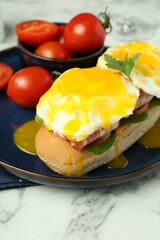 Tasty brunch. Poached eggs, bacon, bun and tomatoes on white marble table, closeup