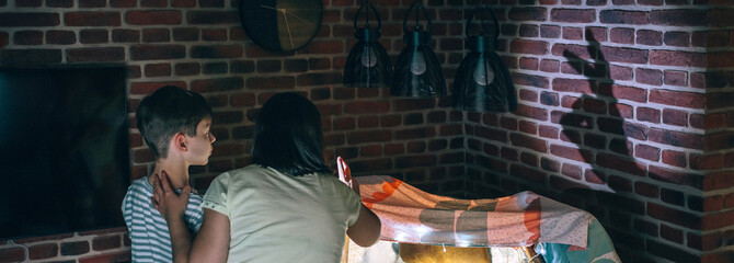 Banner of mother and child having fun playing with shadow puppets over brick wall at home pajama...