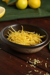 Lemon zest in bowl on wooden table, closeup