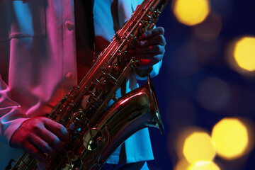 Obraz premium Professional musician playing saxophone on blue background with blurred lights, closeup. Bokeh effect