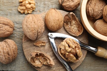Fresh walnuts and nutcracker on wooden table, flat lay