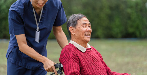 Caregiver smiling while pushing elderly man in wheelchair through a beautiful garden on a sunny day