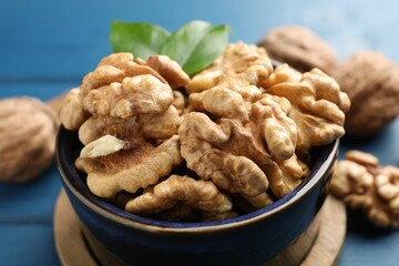 Fresh walnuts in bowl on blue table, closeup