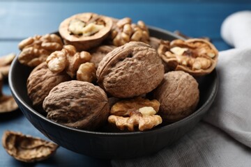 Fresh walnuts in bowl on blue table, closeup