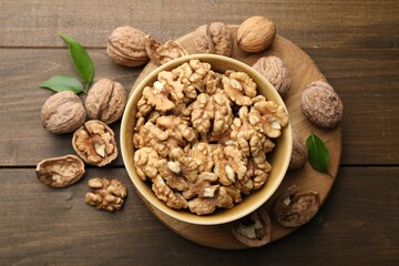 Peeled walnuts in bowl and whole ones on wooden table, flat lay