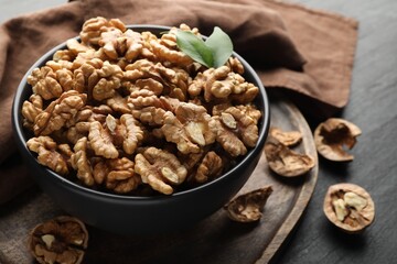 Fresh ripe walnuts in bowl on black table, closeup
