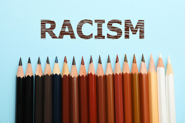 Stop racism. Pencils in different colors on light blue background, top view