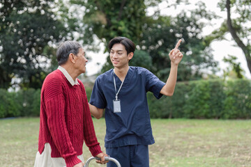 Naklejka premium Nurse joyfully explaining something to elderly man with walker in a vibrant garden setting
