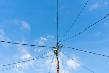 Electric poles with tangled wires and blue sky with fluffy white clouds