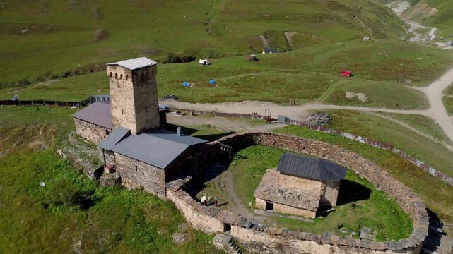 Lamaria Monastery Complex, standing among green meadows in historic village of Ushguli, with stone walls and tower in picturesque Svaneti region of Georgia Drone Footage.